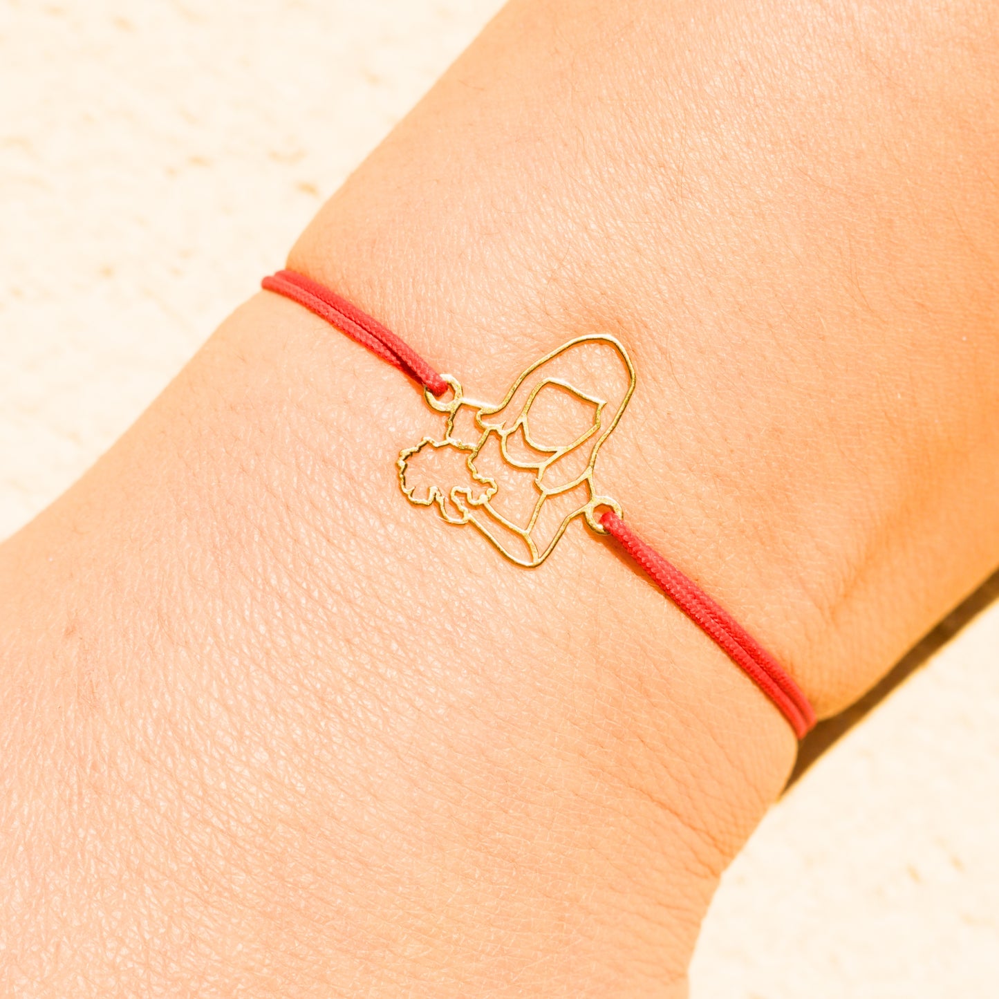 Bracelet personnalisé en or avec cordon rouge, porté au poignet, créé à partir d’une photo de fillette tenant un bouquet.