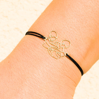 Bracelet sur mesure Stydor porté au poignet, en or avec cordon noir, transformé à partir d’une photo d’enfants et d’un bébé.